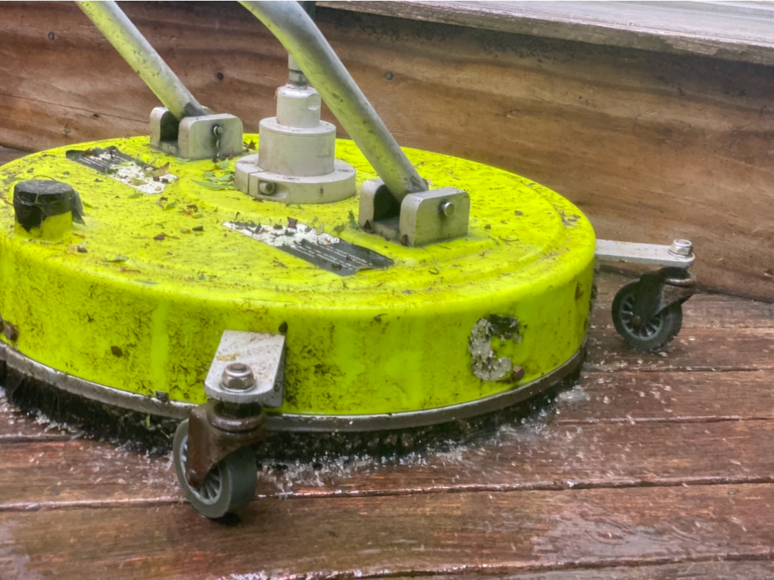 Technician using a machine to clean a deck, removing dirt and stains with powerful cleaning equipment.