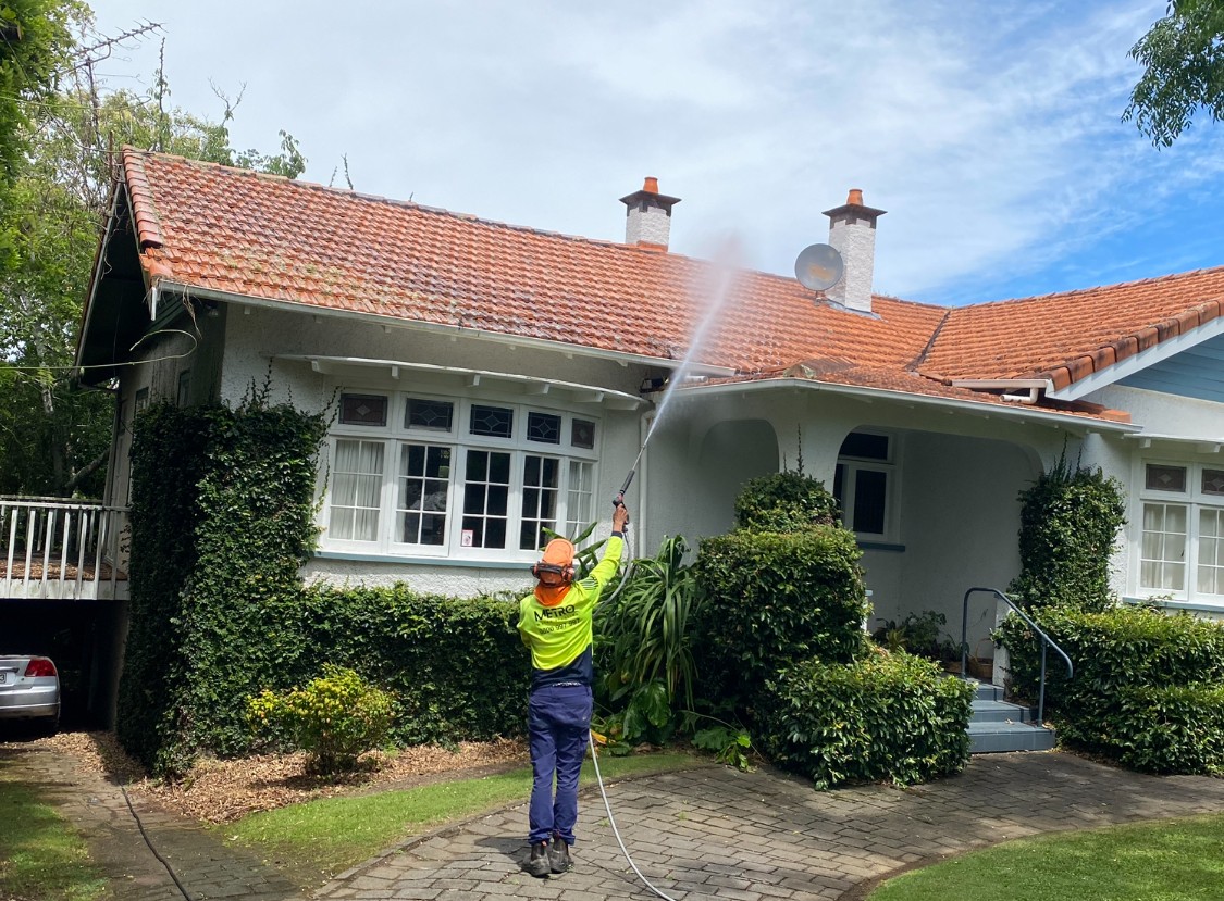 Metro Water Blasting technician applying moss and mould treatment on a residential roof in Auckland.
