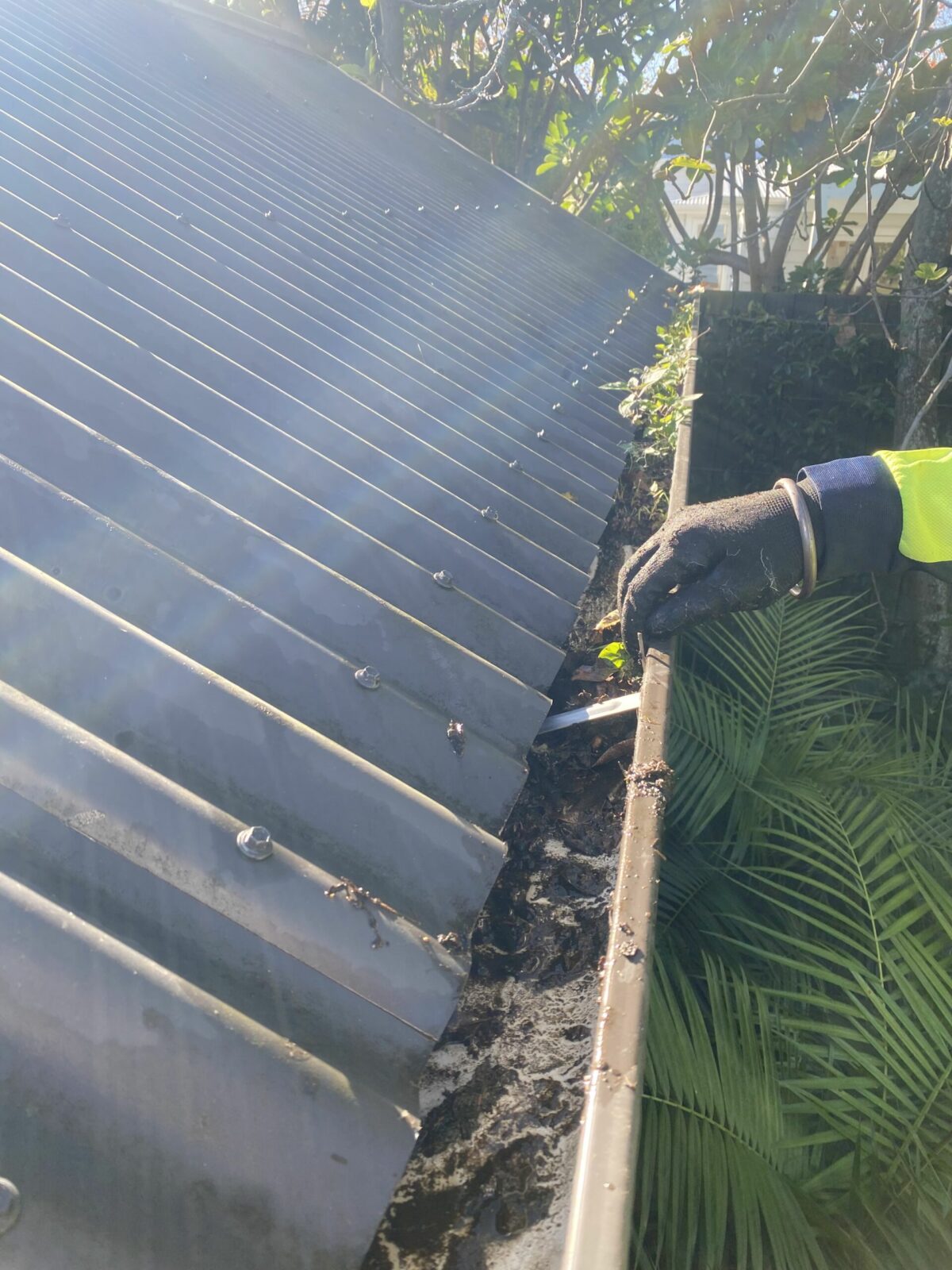 Metro Water Blasting technician hand-removing debris from residential gutters during cleaning service.