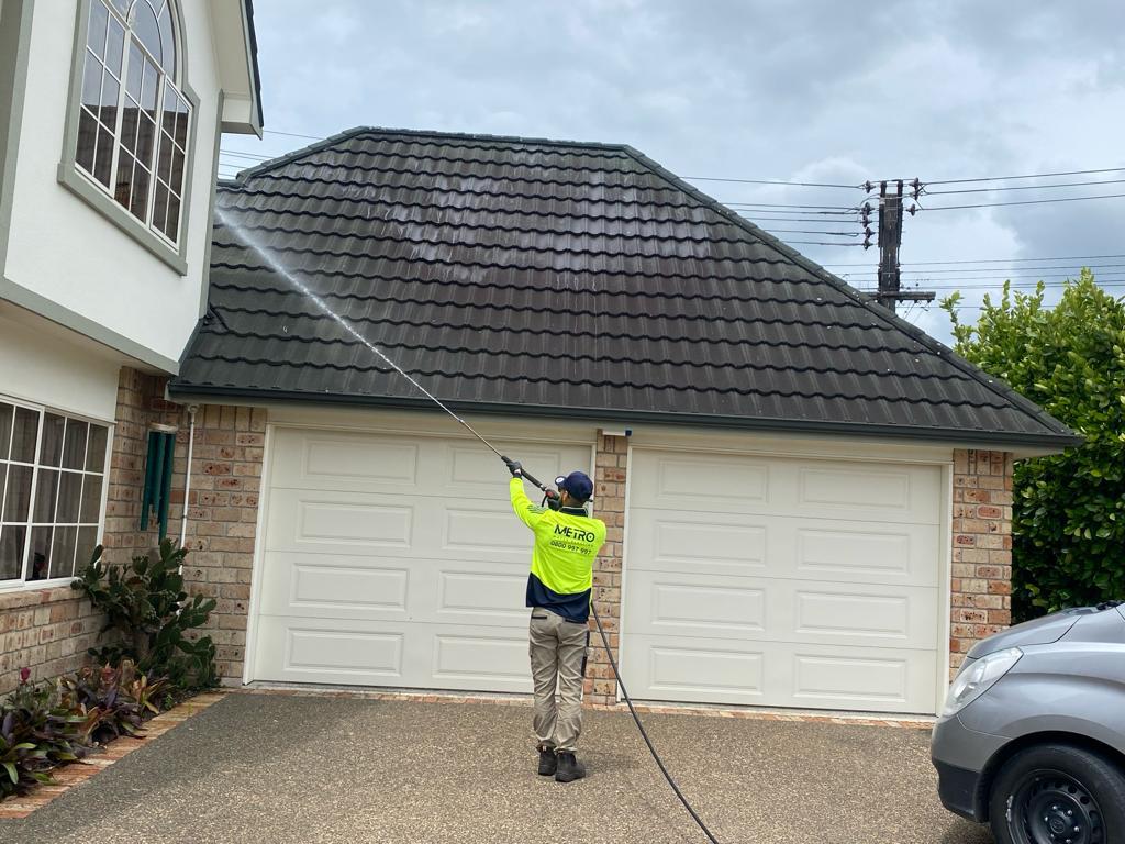 Metro Water Blasting technician spraying moss and mould treatment onto a residential roof.